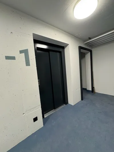 Frisch gestrichene Tiefgarage in Winterthur mit Aufzug, hellen Wänden und blauer Bodenbeschichtung – präzise Malerarbeiten vom Malerbetrieb in Winterthur.